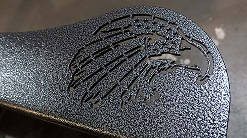 A photo of an eagle design cut into the arm of a steel bench