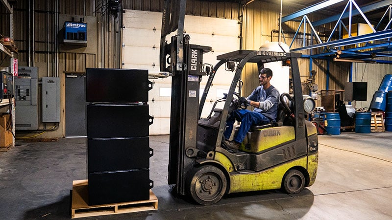 Employee using a forklift to move newly manufactured mine battery cases.